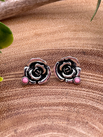 Silver rose-shaped earrings with pink accent on a brown surface