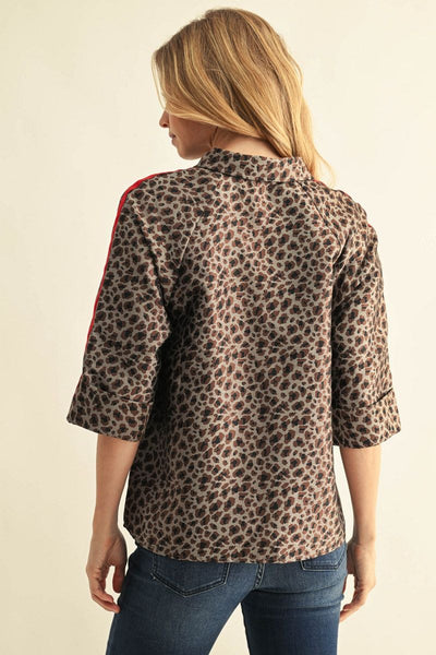 A woman shown from the back wearing a leopard print button-up shirt with red stripes down the sleeves and blue jeans, set against a plain beige background.