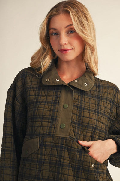 A woman wearing a quilted plaid jacket in olive green and black, featuring a wide collar with snap buttons and a snap-button placket, photographed against a plain light background.