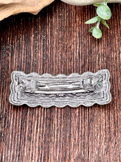 Silver hair clip on a wooden surface with green leaves