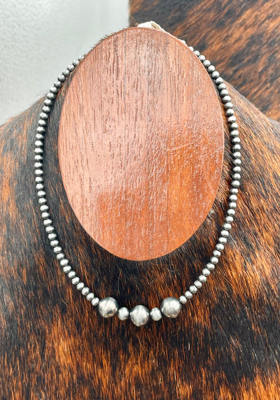 Silver beaded necklace on a wooden stand with a brown and black background