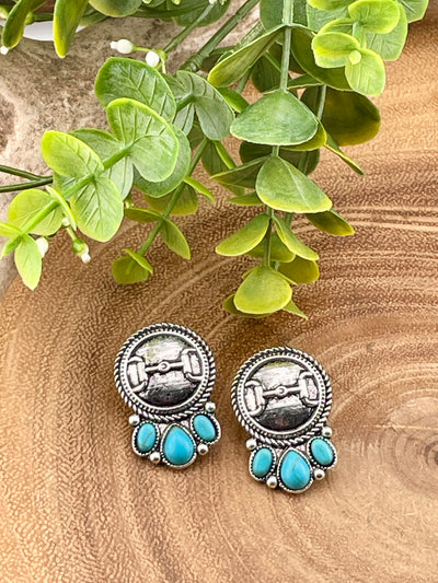 Pair of silver and turquoise earrings on a wooden surface with green leaves.