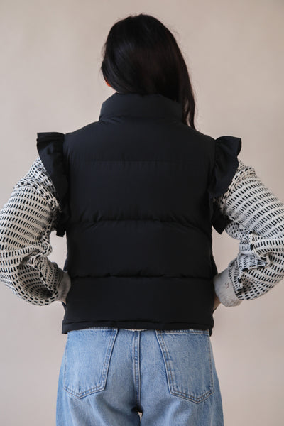 Person wearing a black puffer vest over a patterned shirt with a neutral background