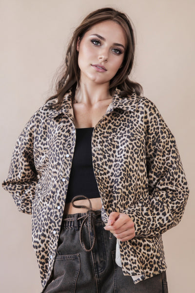 Woman wearing a leopard print jacket over a black top and gray pants on a beige background