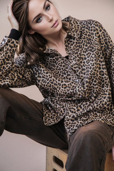 Woman wearing a leopard print blouse sitting on a wooden stool.