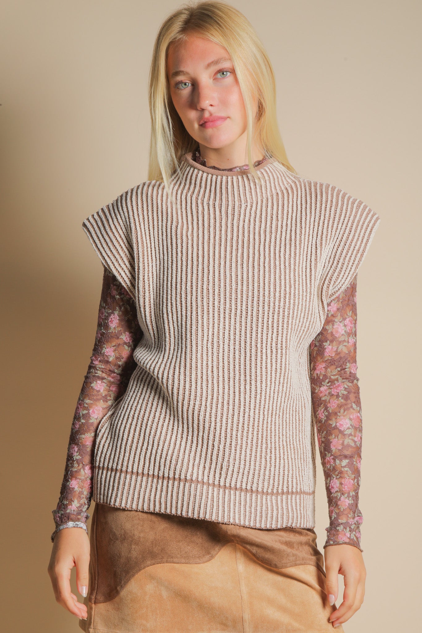 Woman wearing a sleeveless knitted top with floral sleeves against a beige background