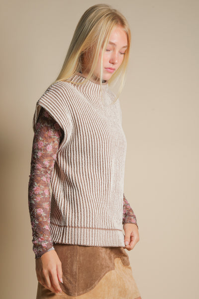 Woman wearing a ribbed knit vest over a patterned long-sleeve shirt on a beige background