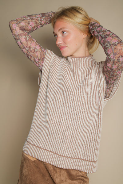 Woman wearing a patterned sleeveless top over a beige vest against a plain background