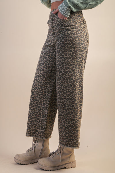 Person wearing leopard print pants and beige boots on a plain background