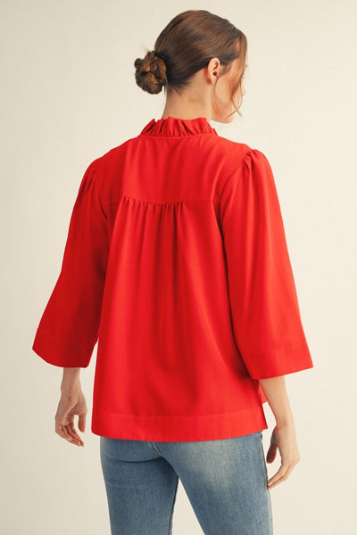 back of model wearing a red blouse & jeans with tan background