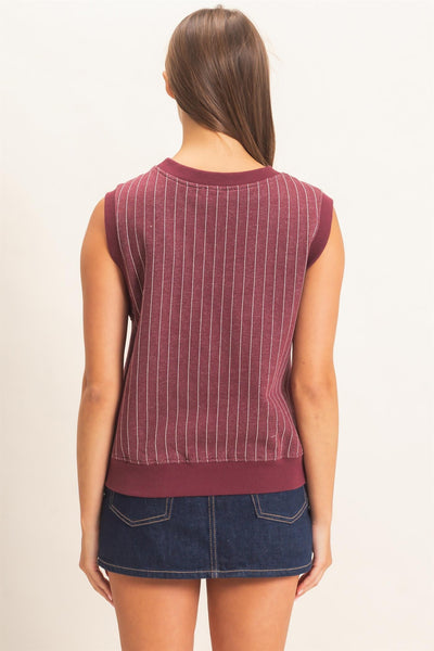 back of a model wearing a burgundy striped v neck sleeveless top with a jean skirt on a light background
