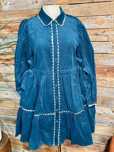 teal corduroy dress with white scalloped detail on a mannequin in front of a wooden slat wall
