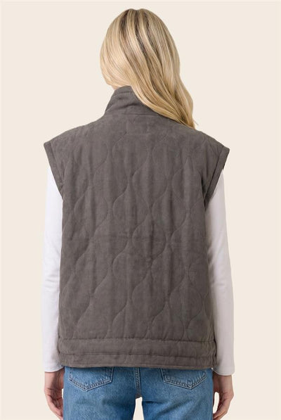 back of model wearing a white top & jeans with a charcoal vest and a light background