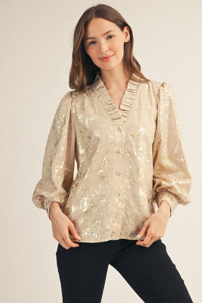 Woman wearing a beige metallic blouse with black pants on a plain background
