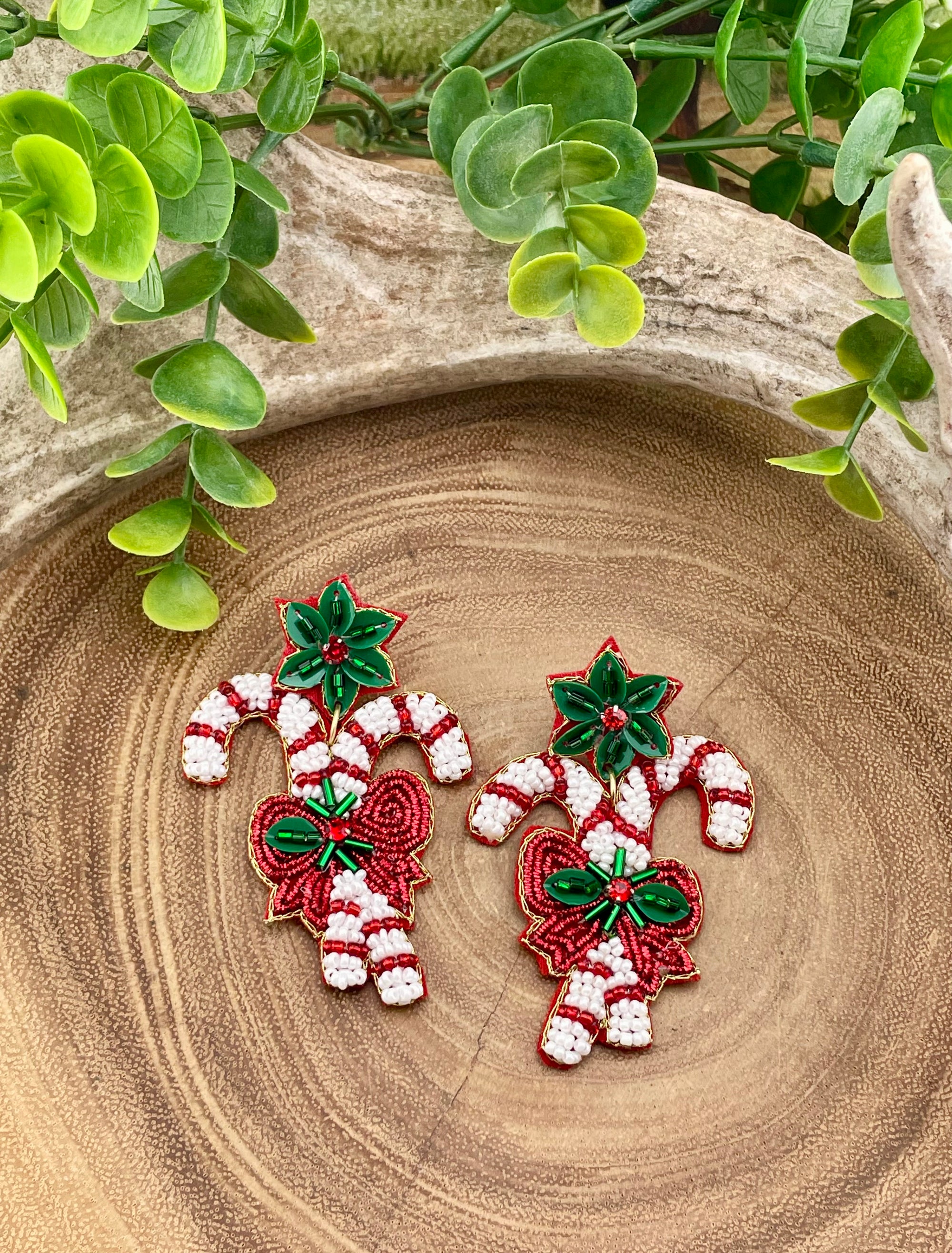 Two candy cane-shaped earrings with green leaves on a wooden surface.