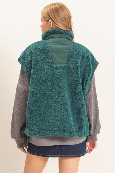 back of a model wearing a gray shirt and jeans skirt with a green Sherpa Vest over it.