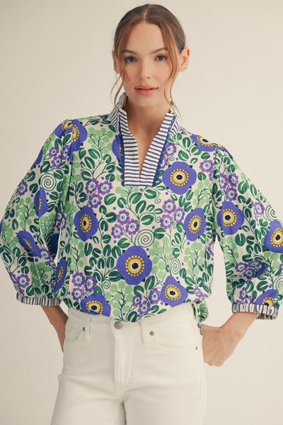 model wearing blue stripe & floral blouse with white pants on a light background