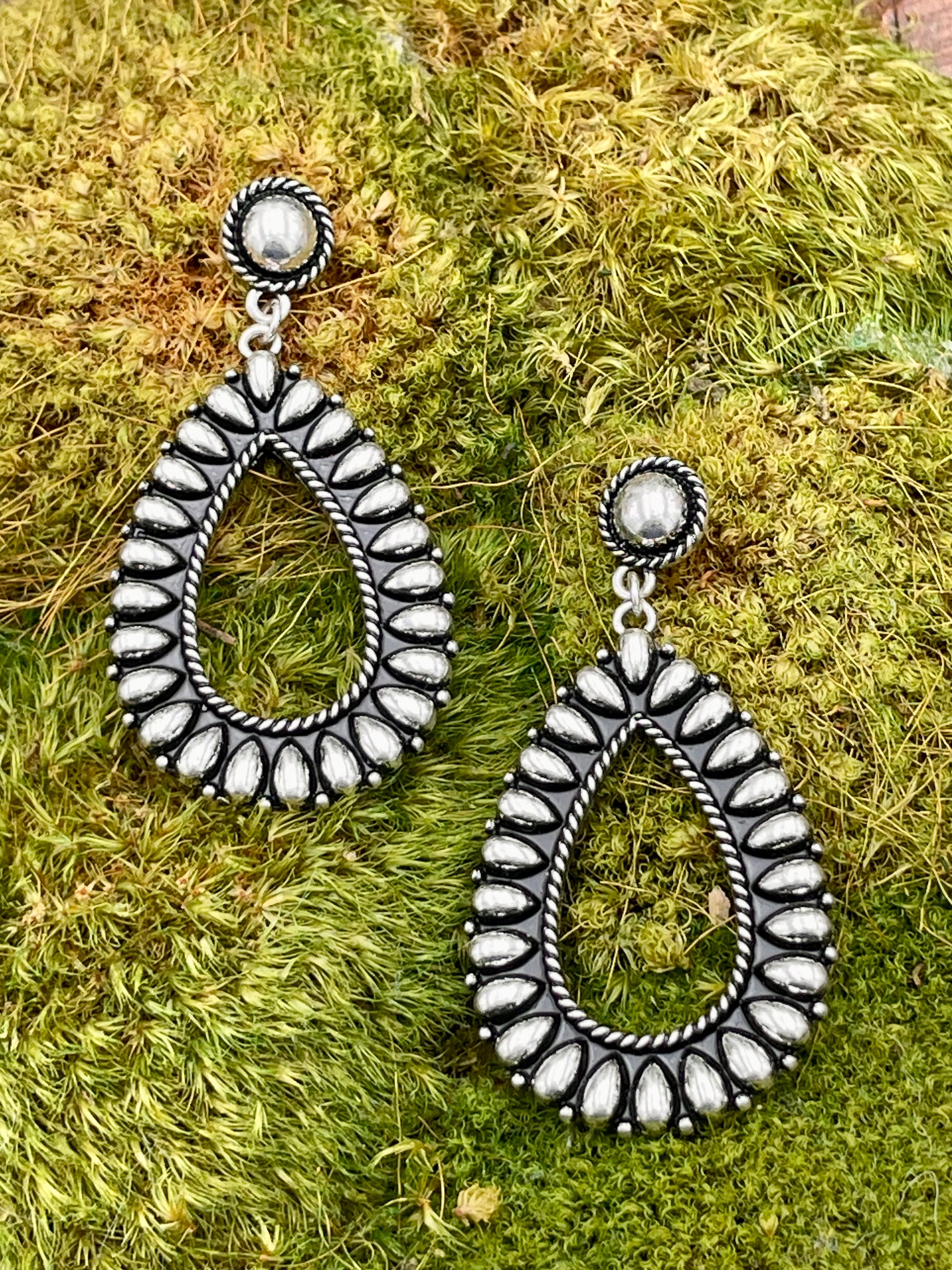 Pair of silver teardrop earrings on a green grass background