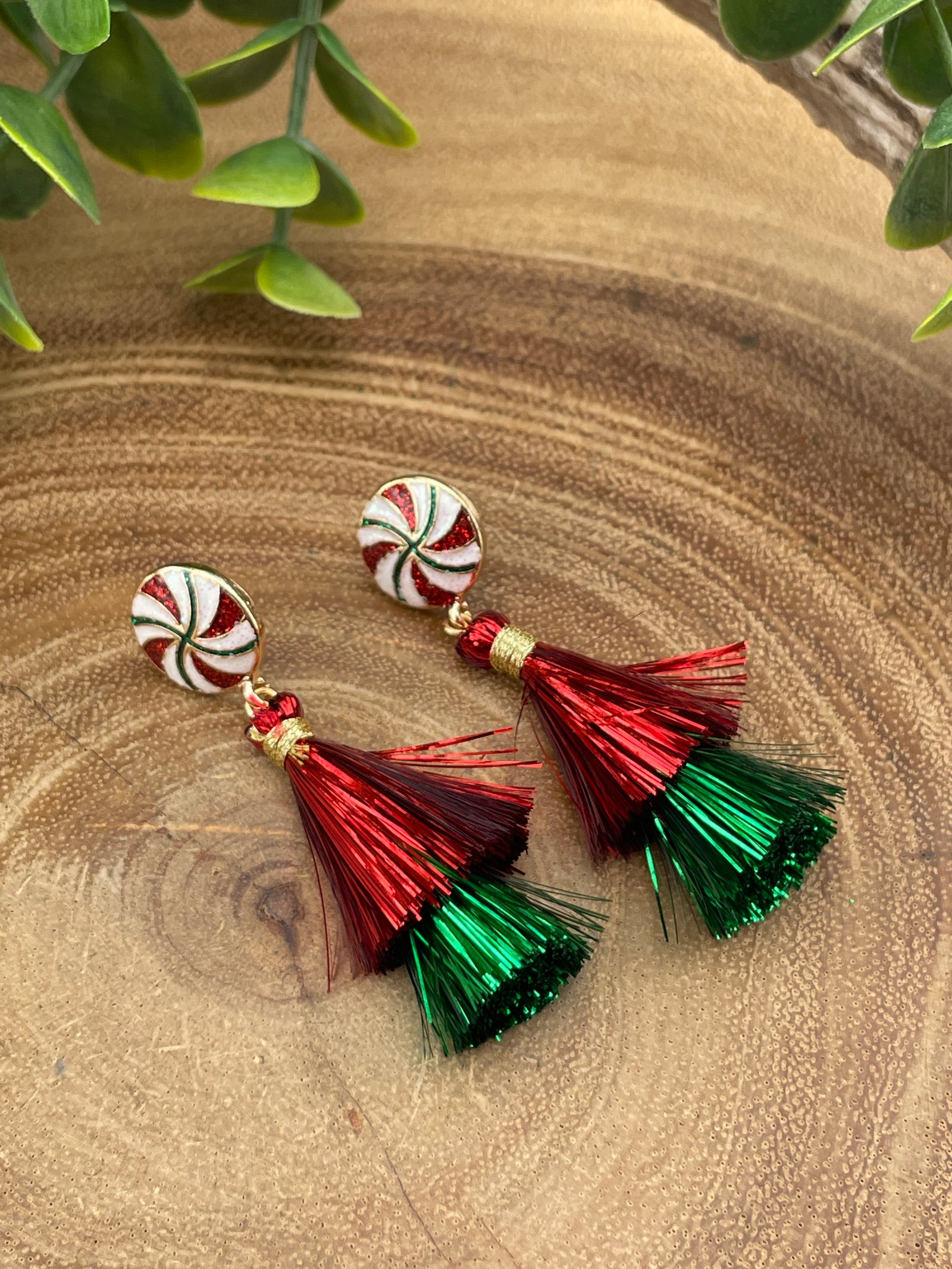 Pair of earrings with red and green tassels on a wooden surface