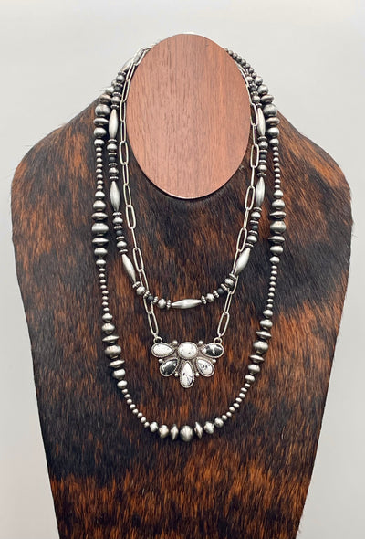 Silver beaded necklace on a wooden mannequin bust against a gray background