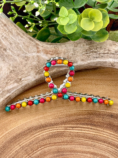 Decorative hair clip with colorful beads on a wooden surface with greenery in the background