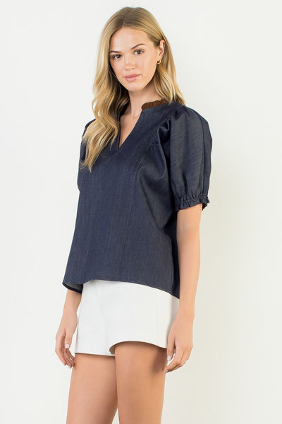 Woman wearing a navy blue blouse with puff sleeves and white shorts on a white background