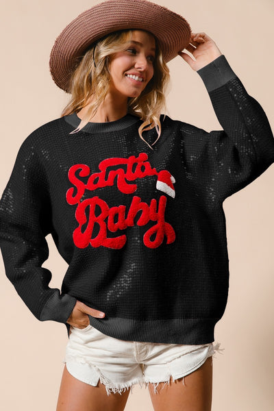 Person wearing a black sweater with 'Santa Baby' in red text, white shorts, and a straw hat on a beige background