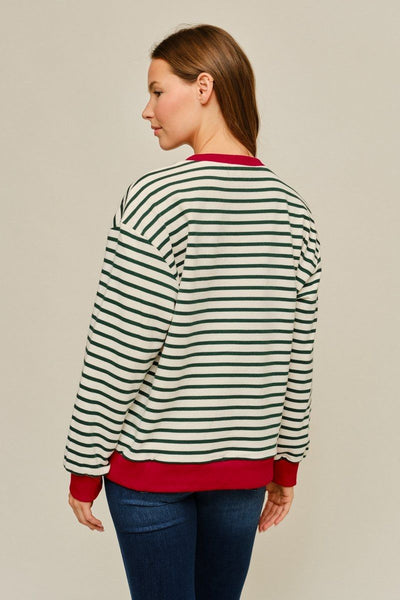 A woman shown from the back wearing a green and white striped crewneck sweatshirt with solid red ribbed collar, cuffs, and hem, paired with blue jeans against a plain beige studio background.