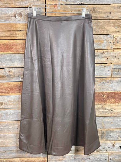 A brown faux-leather midi skirt hanging on a clear plastic hanger against a rustic wooden plank wall.