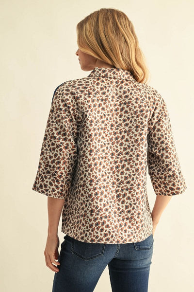A woman shown from the back wearing a leopard print three-quarter sleeve button-up shirt and blue jeans against a plain beige background.