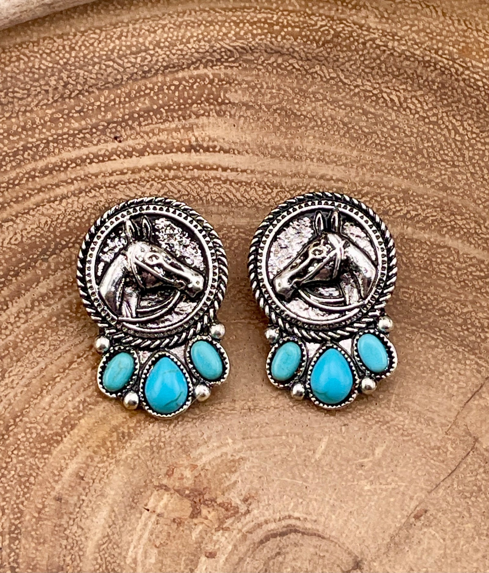 Pair of silver and turquoise horse earrings on a wooden surface