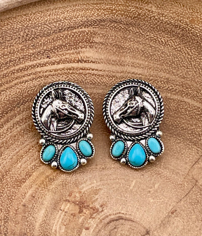Pair of silver and turquoise horse earrings on a wooden surface