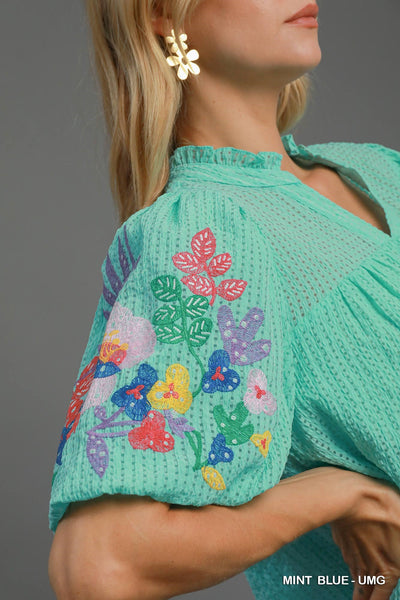 Green embroidered top with colorful floral patterns on a gray background