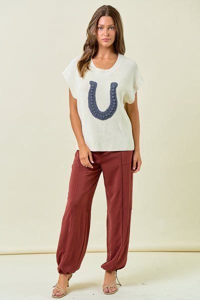 Woman wearing a white t-shirt with a blue graphic and red pants on a beige background