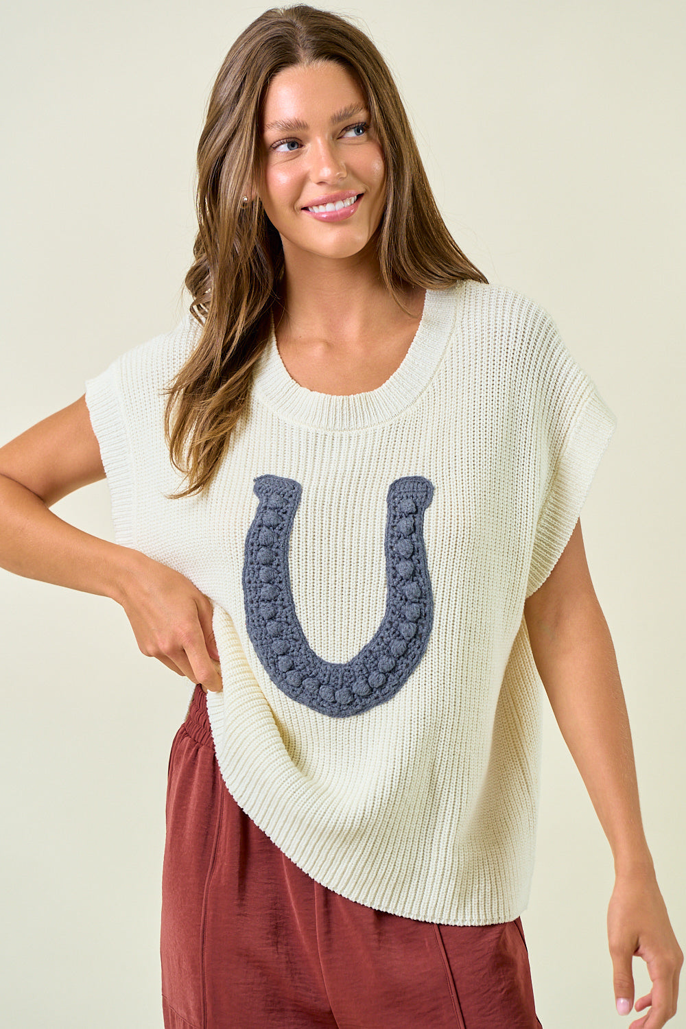 Woman wearing a cream-colored sweater with a blue horseshoe design on a beige background