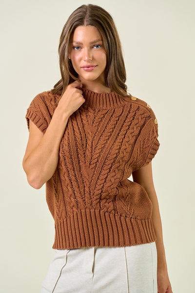 Woman wearing a brown knitted sleeveless sweater against a plain background