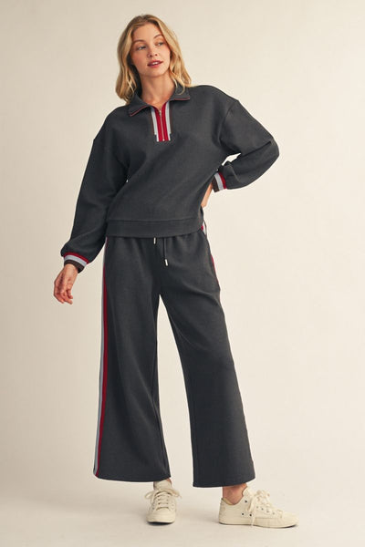 model wearing charcoal sweatshirt & sweatpants with tennis shoes before a beige background