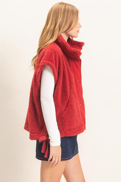 side view of a model wearing white shirt and jeans skirt with a red Sherpa Vest over it.