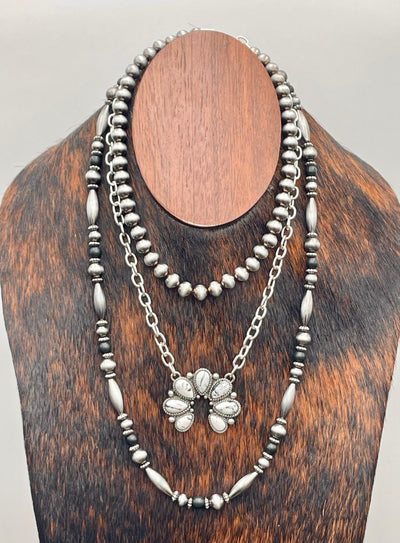 Silver beaded necklace with a white buffalo pendant on a wooden stand.