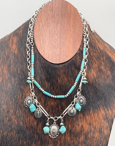 Turquoise beaded necklace with silver charms on a wooden block