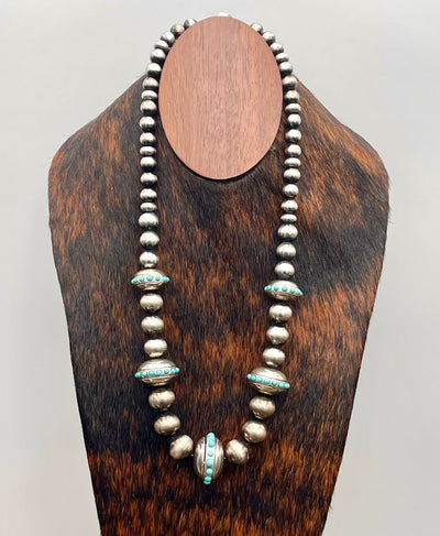 Silver beaded necklace with turquoise accents on a wooden stand against a white background