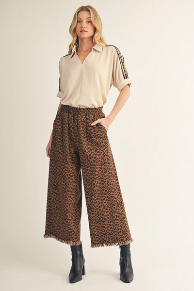 model wearing a tan top with leopard shoulder detail and cropped leopard pants and black boots with a light background