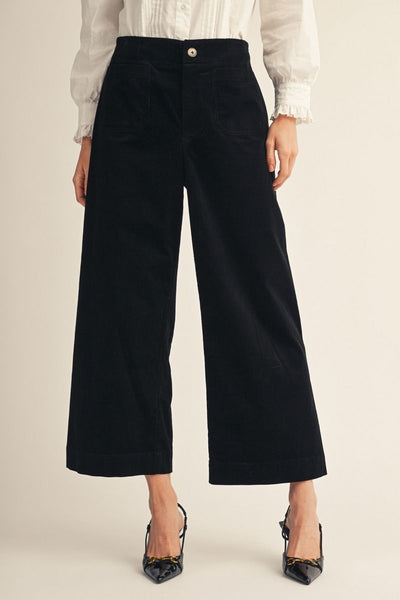 model wearing a white blouse, black heels and black corduroy pants on a beige background