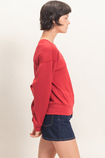 model wearing a red sweatshirt with a jean skirt shows from the side before a light background