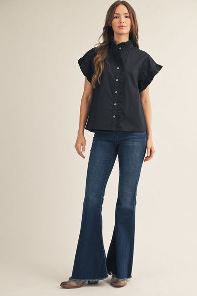 A woman modeling a black short-sleeve button-front blouse with ruffled sleeves and dark blue flare jeans against a plain beige studio background.