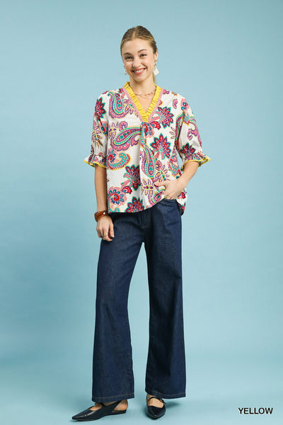 Woman wearing a colorful patterned blouse and blue jeans on a light blue background