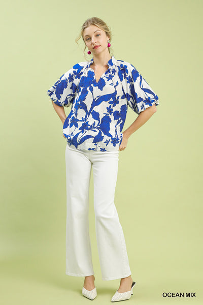 Woman wearing a blue floral blouse and white pants on a light green background