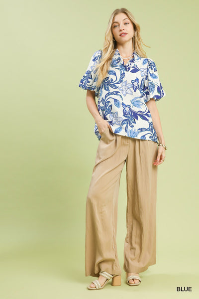 Woman wearing a blue floral blouse and beige pants on a light green background