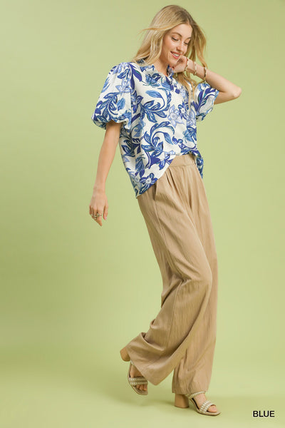 Woman wearing a blue floral top and beige pants on a light green background