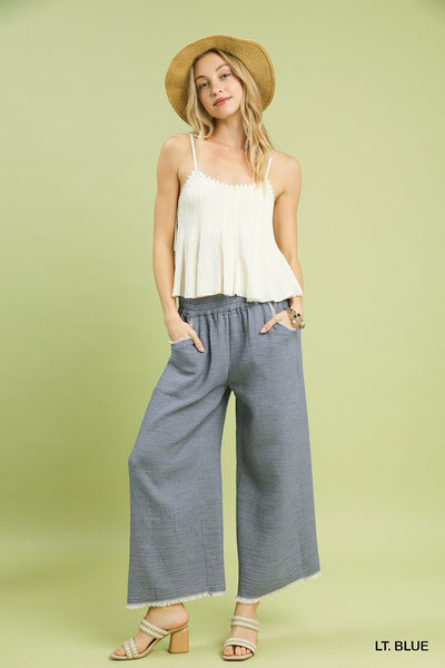 Woman wearing a light-colored top and blue pants with a straw hat on a green background